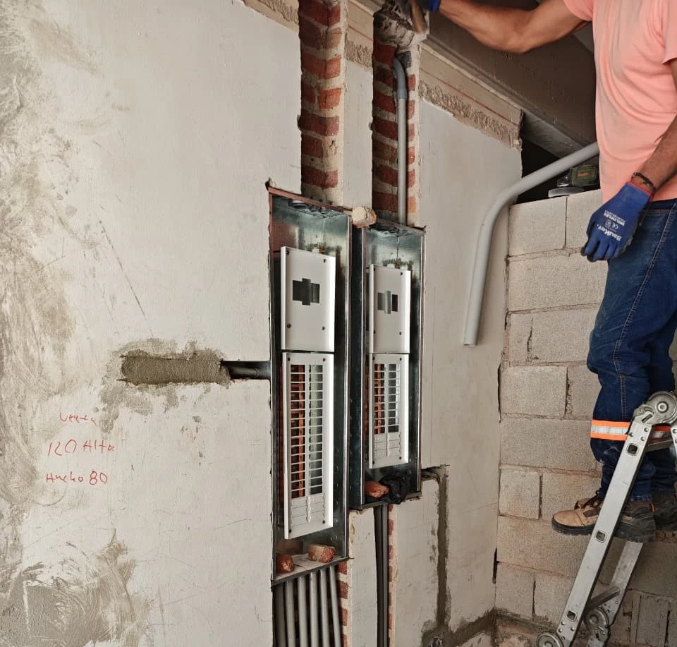 Técnico electricista realizando la instalación de cajas de medidores y ducterías empotradas en muro de construcción para acometidas eléctricas.
