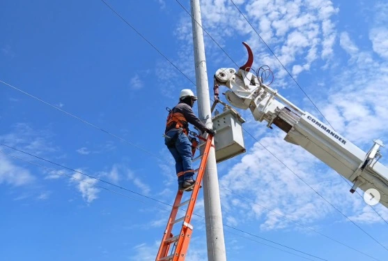 Instalación de transformador de distribución en poste de concreto mediante grúa telescópica y técnico electricista con equipo de protección para alturas.